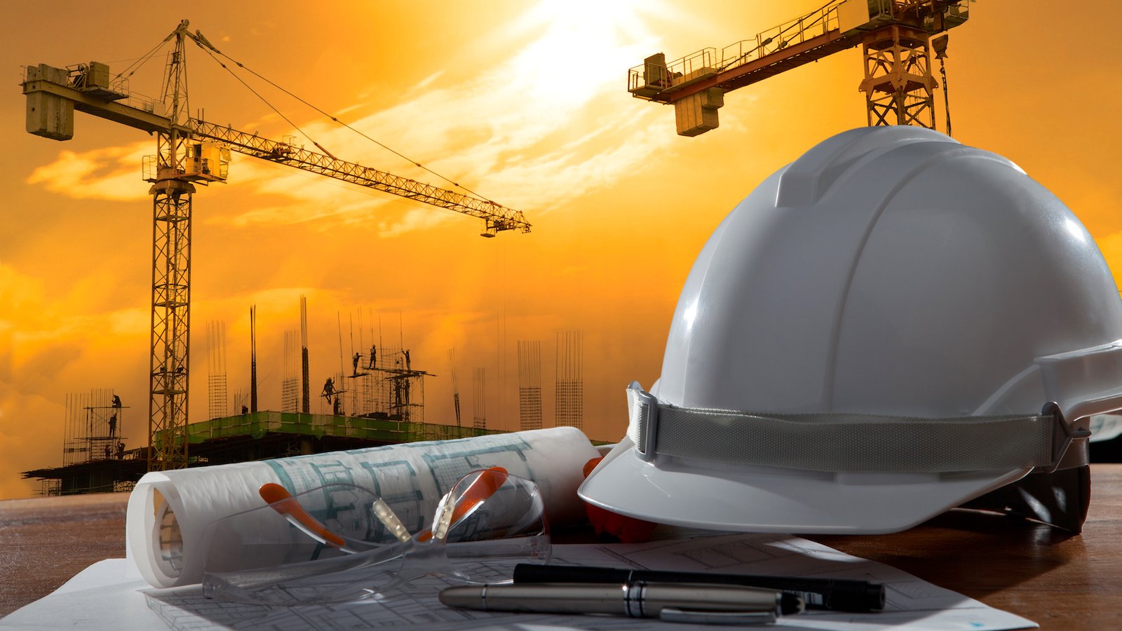 About safety helmet and architect pland on wood table with sunset scene and building construction